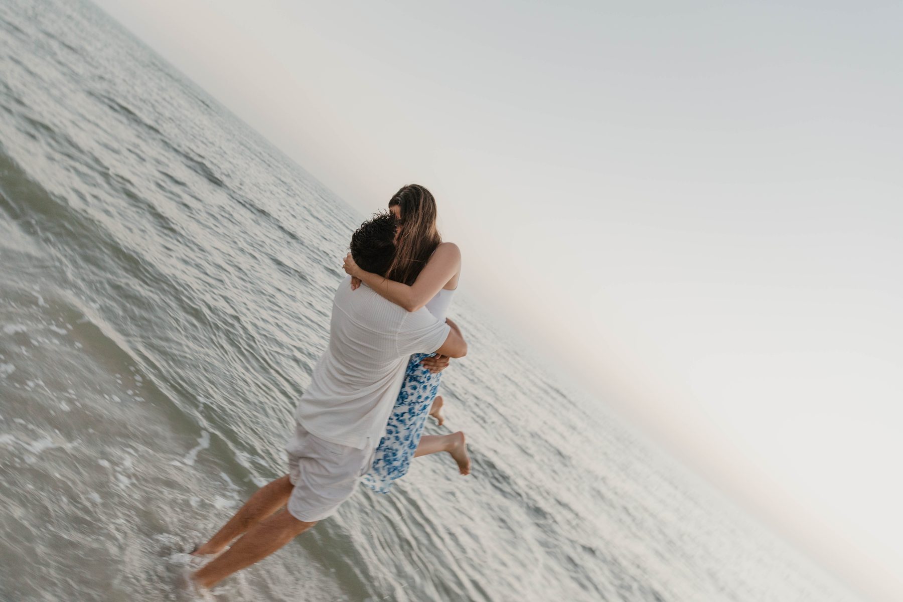 Couple embracing in the ocean shallows at sunset after a beach proposal — Dejeu Crew engagement photography