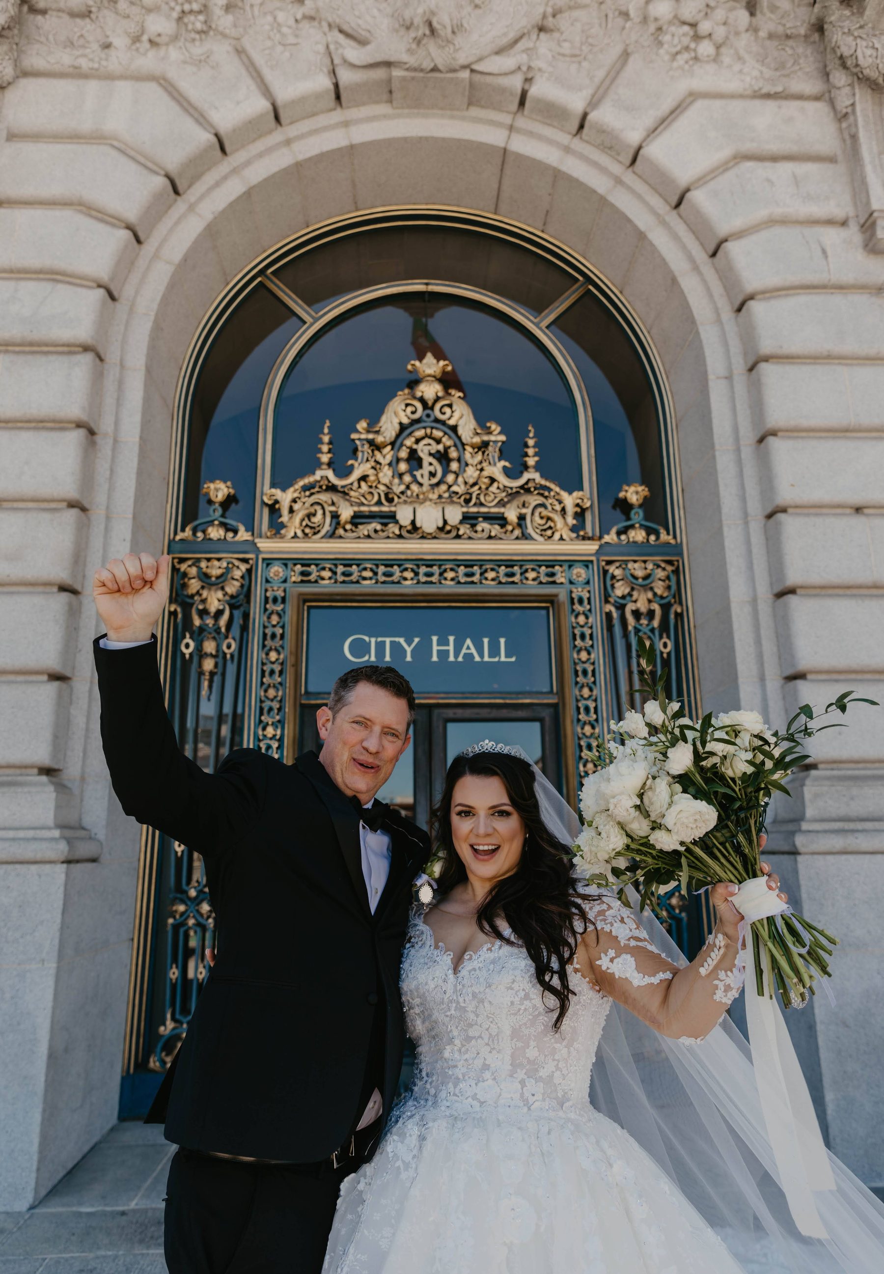 Bride and groom celebrating with a raised bouquet outside City Hall’s gilded doors — Dejeu Crew wedding photography