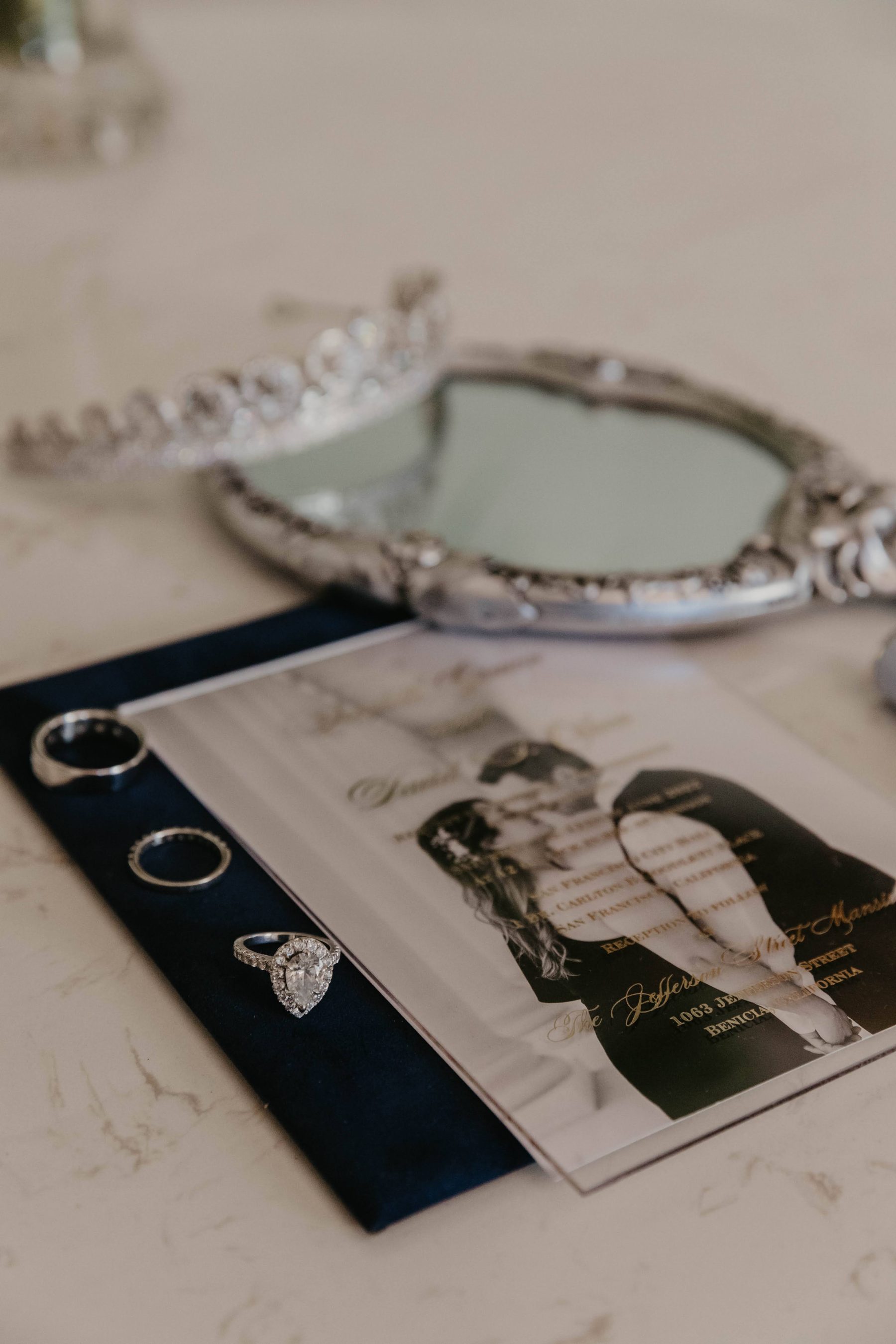 Wedding rings on an invitation card beside a vintage hand mirror — Dejeu Crew wedding photography
