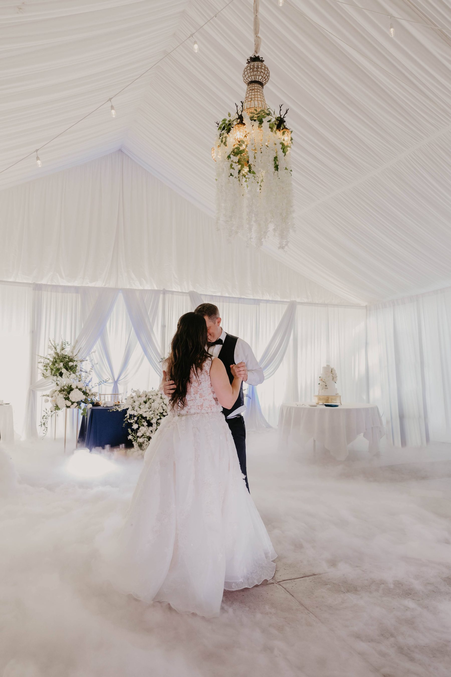 Bride and groom’s first dance under a chandelier in a white tented reception — Dejeu Crew wedding photography