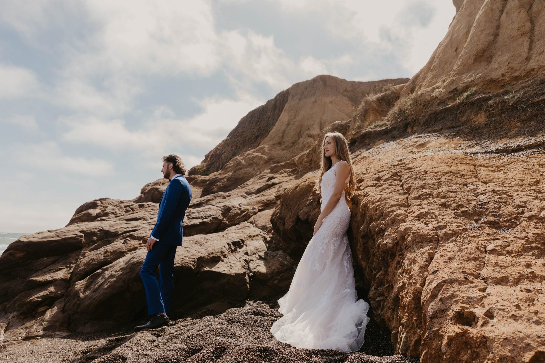 Bride leaning against sandstone rocks as the groom looks out over the coast — Dejeu Crew wedding photography