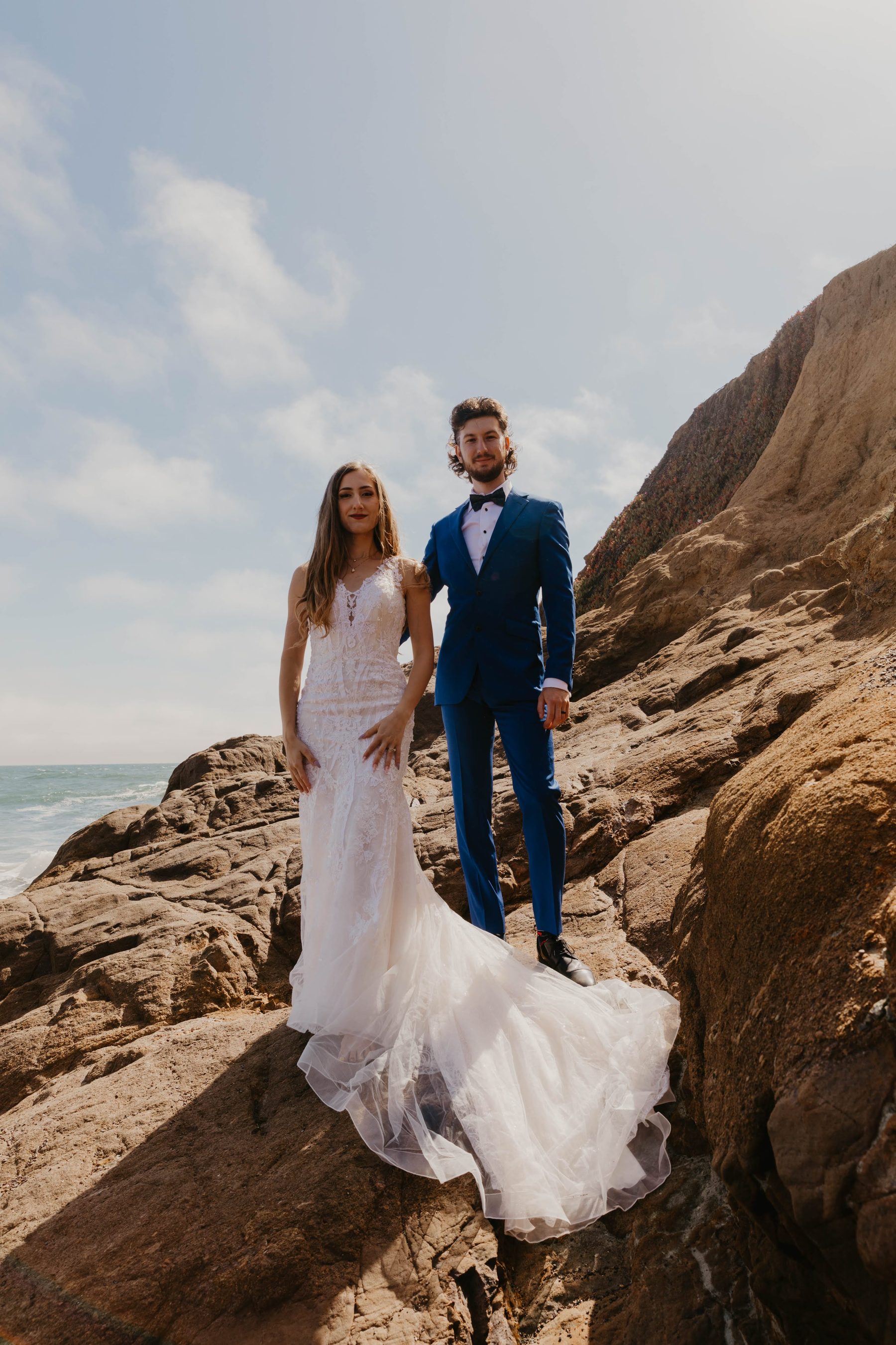 Bride and groom standing together on sunlit coastal bluffs under a blue sky — Dejeu Crew wedding photography