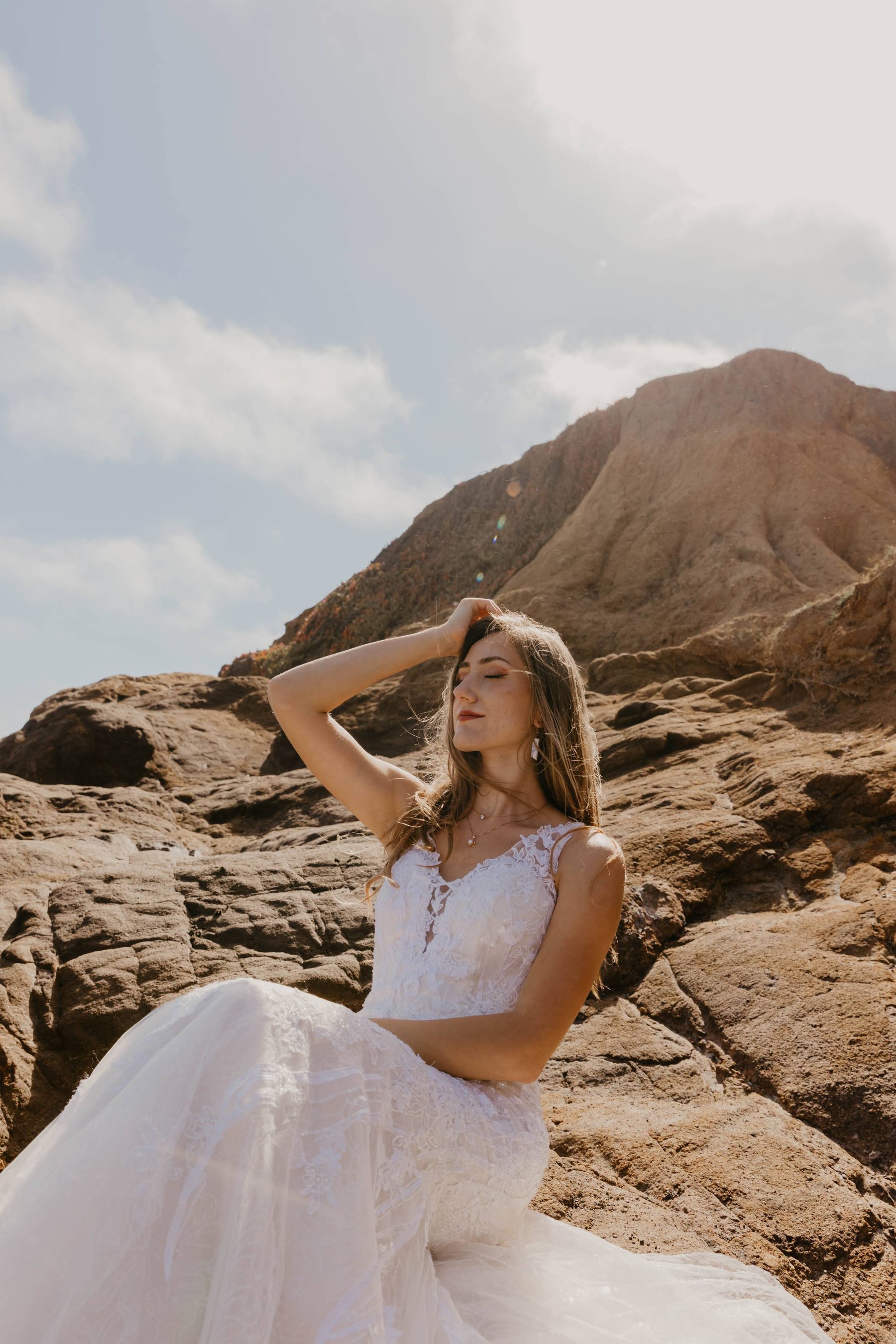 Bride with her hand in her hair, posing on sunlit sandstone bluffs — Dejeu Crew wedding photography