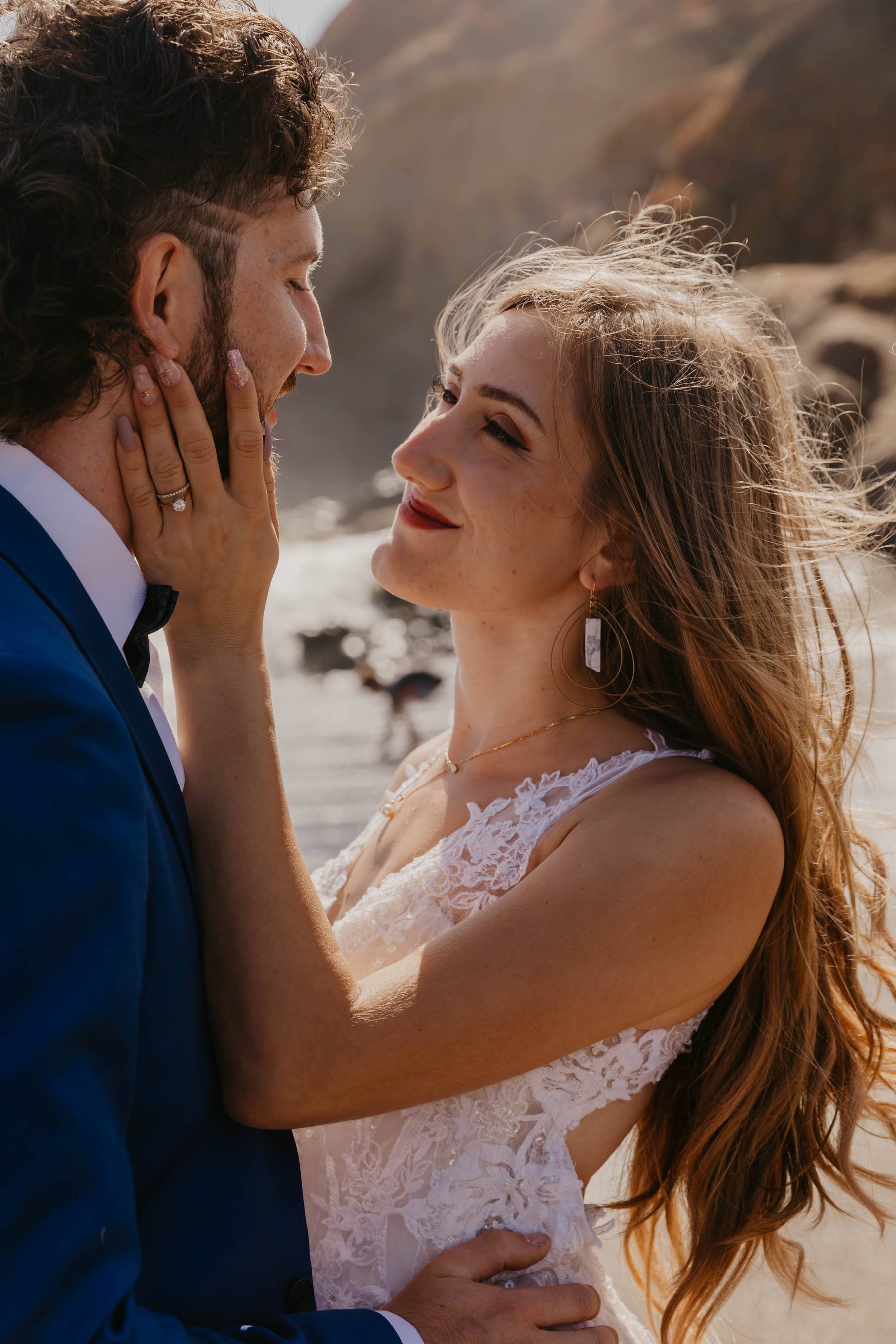 Groom cupping the bride’s face as she gazes up at him, hair blowing in the wind — Dejeu Crew wedding photography